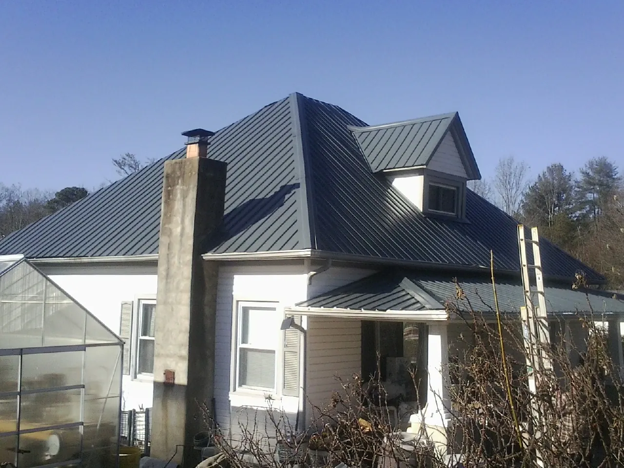Dark blue standing seam metal roof on a white farmhouse with dormer — Slate & Tile Roof Repair by Roofing Brothers in Peck
