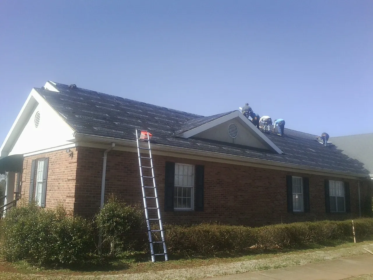 Crew tearing shingles off a brick ranch roof with a ladder set — Emergency Roof Repair work by our crew in Peck