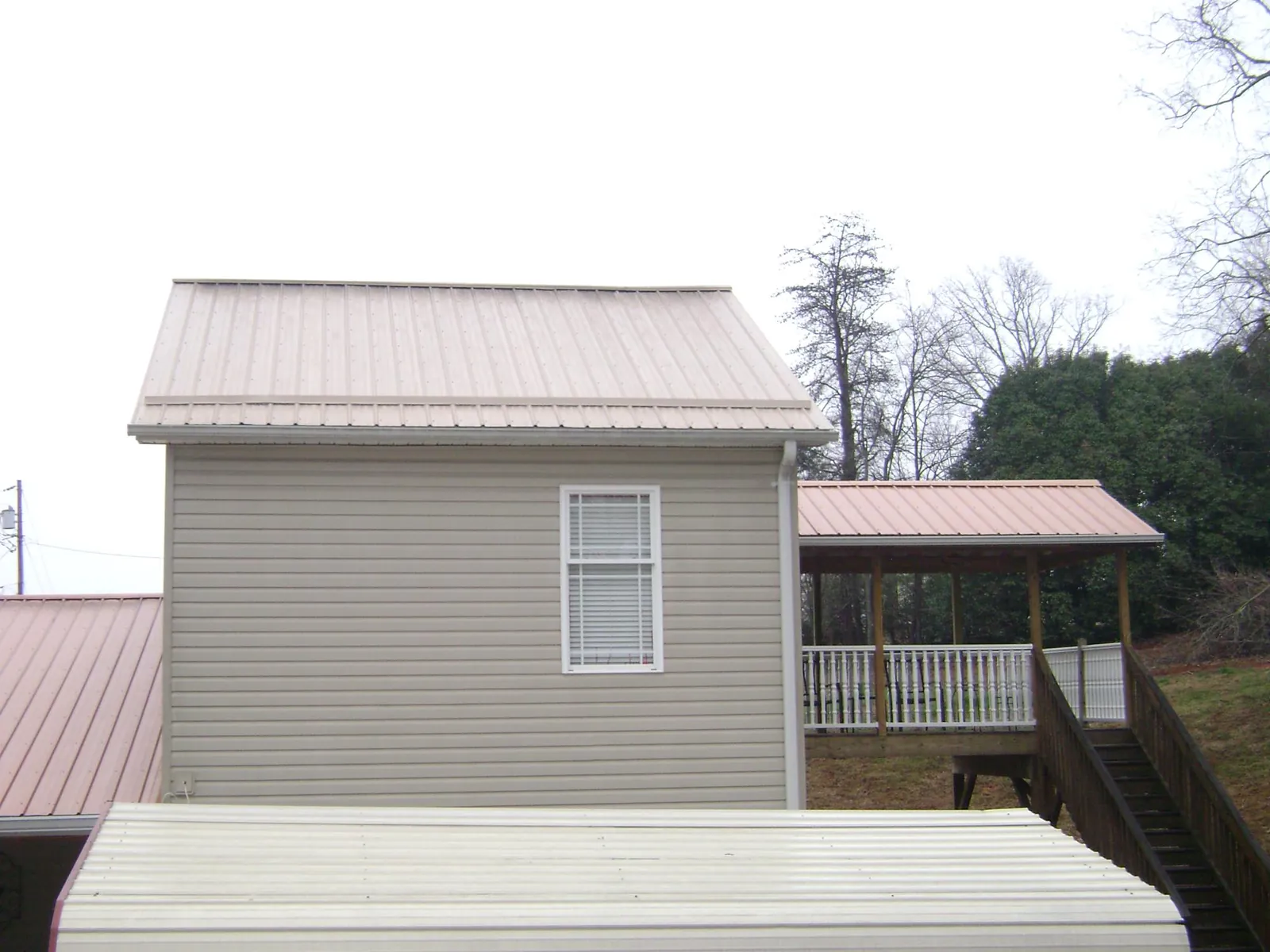 Tan metal roofs on a two story addition and attached porch, from a Roof Replacement job in Peck